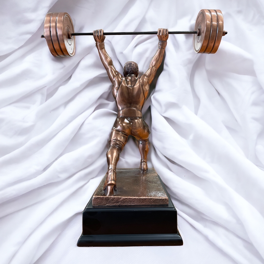 Our Overhead Press Trophy shown from back view. It shows the straining muscles of the lifters back, glutes & quads. The bronze statue of the lifter is mounted on a wood base. The trophy is sitting in front of a wrinkly white sheet to help contrast the bronze powerlifter & black wood base.