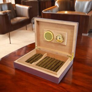 Our Personalized Humidor shown sitting on a piano finished table with leather chairs in the back ground. The humidor is shown with the lid open. The inside of the lid shows a hygrometer and a humidifier. The bottom of the box if filled with cigars. The inside of the box is made with Spanish Cedar, while the outside has a rosewood piano finish. This HMD01 is 9.5" x 7.25" in size and weighs 2.2 lbs.