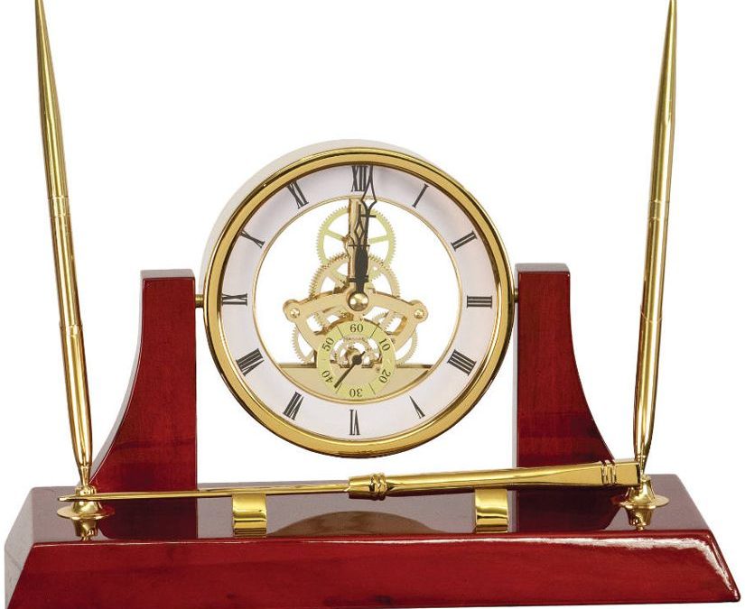 An Executive Gold Clock Desk Set. It's made with rosewood that's coated with a glossy piano finish. It features 2 gold pens, a letter opener & a gold skeleton clock.