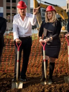 Sir. Richard Branson & Mayor Megan Barry, the Mayor of Nashville. They're standing next to each other wearing red hard hats & holding shovels that are in the dirt as they're at a ground breaking ceremony for Virgin Hotels.