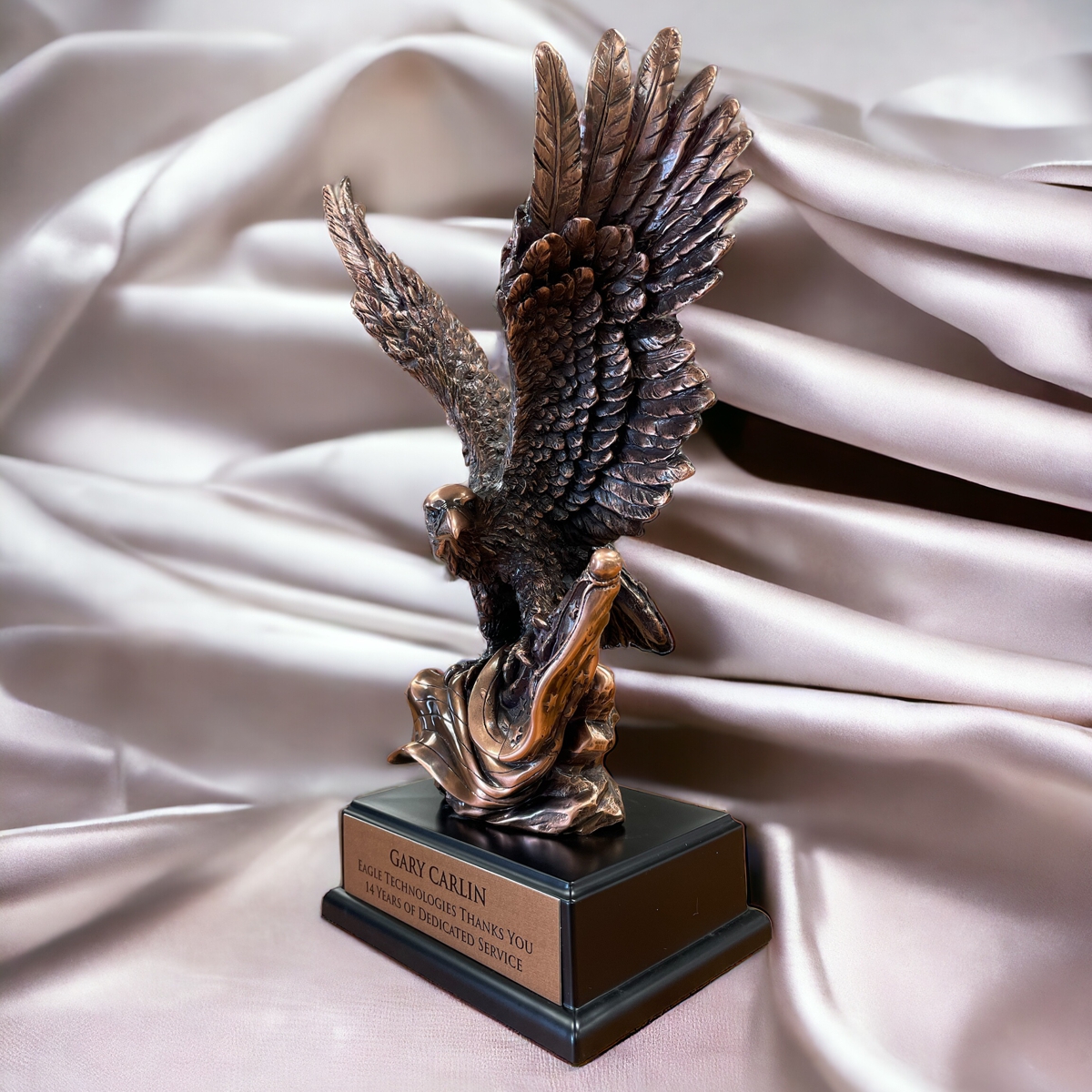 Our Bronze Eagle Statue with a flag facing left in front of a satin background.