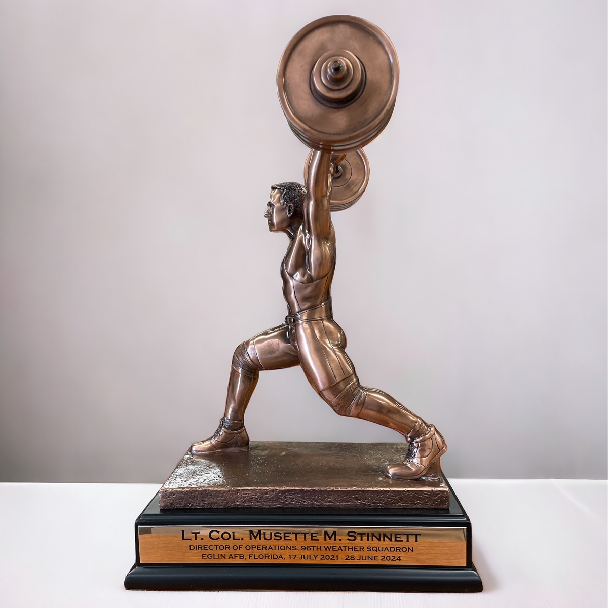 Our Powerlifting Trophy features a weightlifter completing a clean & jerk. It's a resin statue that's coated with a thin bronze metal for added detail & strength. It's mounted on a black wood base with a matching bronze colored engraving plate that can be personalized. This RFB087 trophy is 10" x 14.5" in size and weighs over 7.5 lbs.